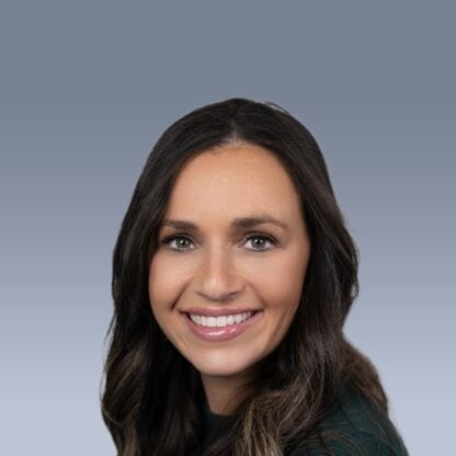 A woman with long dark hair and a green top smiles at the camera against a gradient blue background.