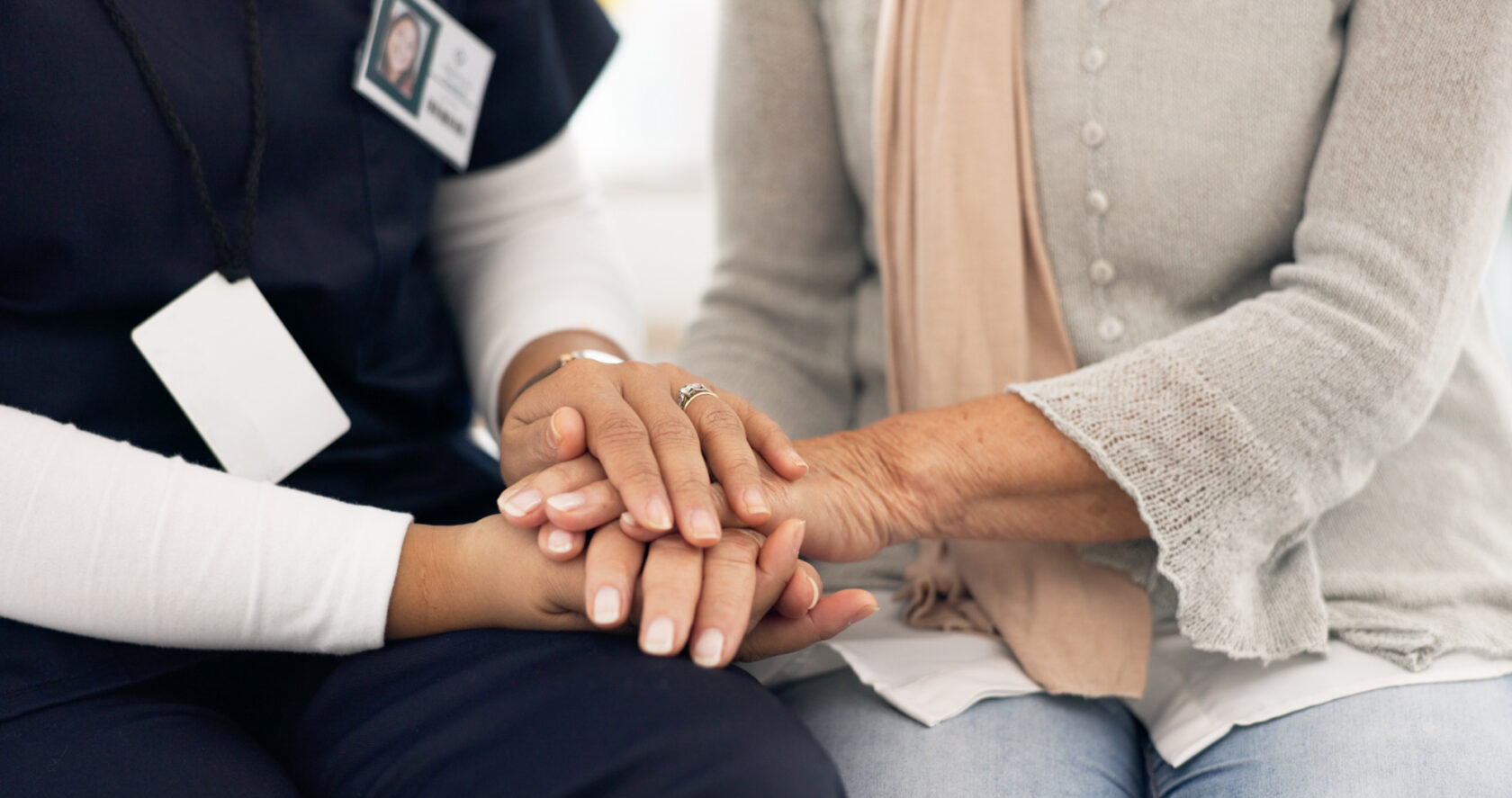 A healthcare worker holds the hand of an elderly woman, conveying care and support as they sit close together.