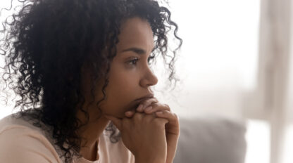 A woman with curly hair looks to the side, her face resting on her clasped hands, in a thoughtful expression.